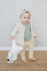 Toddler standing on a rug in Avauma off white cardigan set, holding a white teddy bear Toddler standing on a rug in Avauma off white cardigan set, holding a white teddy bear