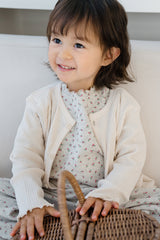 Baby wearing Avauma off white cardigan and beige ribbed pants, sitting on a wooden chair Baby wearing Avauma off white cardigan and beige ribbed pants, sitting on a wooden chair