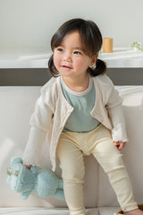 Toddler girl sitting on a couch in Avauma off white knit cardigan and leggings set Toddler girl sitting on a couch in Avauma off white knit cardigan and leggings set