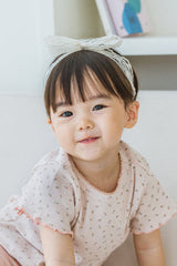 Smiling toddler girl in Avauma Rumiere Ribbon Band and ruffle-sleeve floral tee, sitting in a cozy room Smiling toddler girl in Avauma Rumiere Ribbon Band and ruffle-sleeve floral tee, sitting in a cozy room