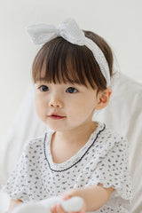 Toddler girl in Avauma Cotton Cream Rumiere Ribbon Band and ruffle-sleeve floral tee, looking gently ahead Toddler girl in Avauma Cotton Cream Rumiere Ribbon Band and ruffle-sleeve floral tee, looking gently ahead