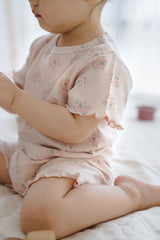 Back view of a toddler girl in Avauma Sienna Rose Rosy Powder floral set, climbing on a white sofa with playful movement. Back view of a toddler girl in Avauma Sienna Rose Rosy Powder floral set, climbing on a white sofa with playful movement.