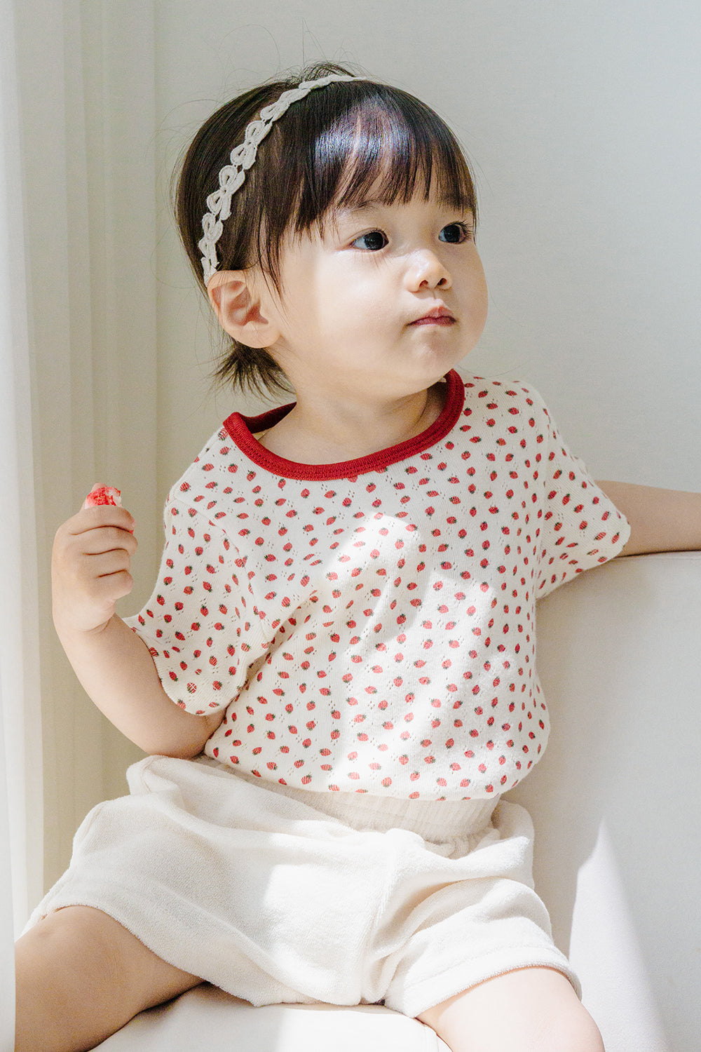 Baby girl in polka dot top wearing Avauma White Garden Band headband in Cream Beige, sitting by the window" Baby girl in polka dot top wearing Avauma White Garden Band headband in Cream Beige, sitting by the window"