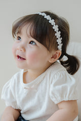 Baby girl wearing Avauma White Garden Band headband in Pure White, sitting on a bed Baby girl wearing Avauma White Garden Band headband in Pure White, sitting on a bed