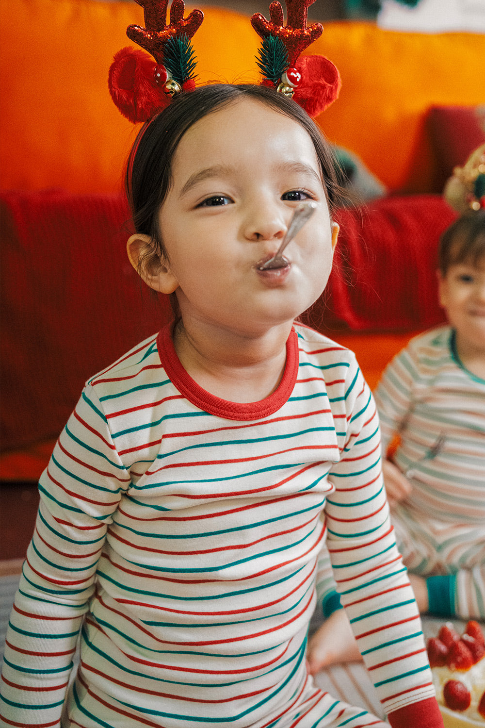 Child wearing AVAUMA Holiday Long Sleeve Pajama Set - Candy Stripe Redcuff, enjoying a holiday snack

