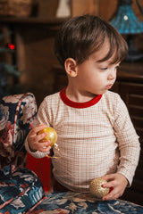 Toddler wearing Avauma Cranberry Check Holiday Pajama Set with festive red details, holding golden Christmas ornaments

