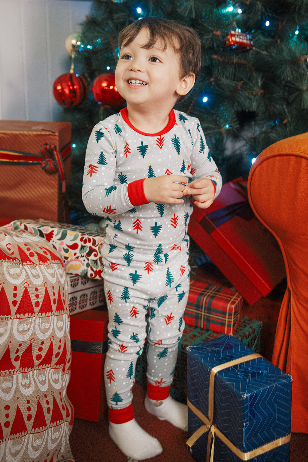 Baby smiling by Christmas tree wearing AVAUMA Holiday Long Sleeve Pajama Set - Happy Tree

