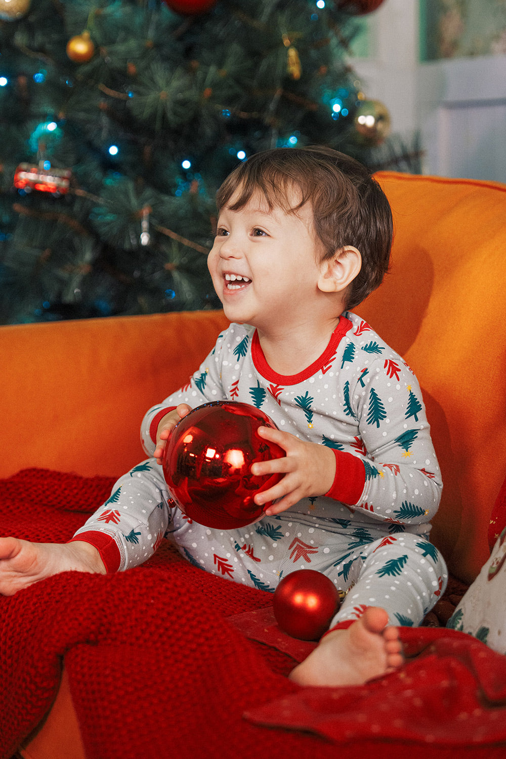 Baby holding Christmas ornament wearing AVAUMA Holiday Long Sleeve Pajama Set - Happy Tree