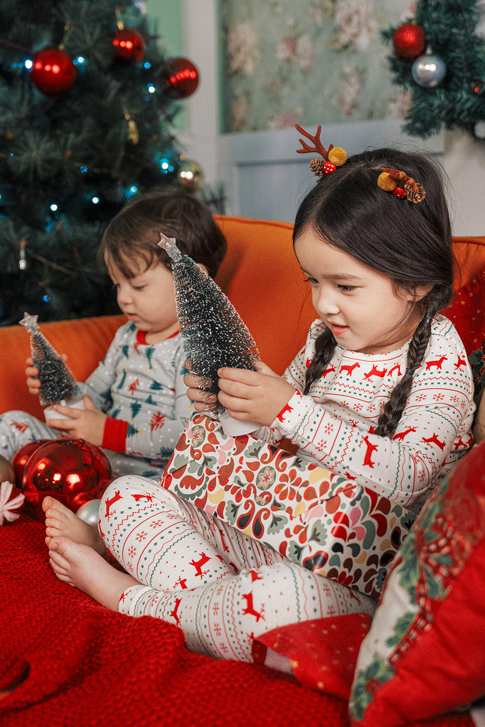 Child with antler headband holding Christmas ornament, dressed in AVAUMA Holiday Long Sleeve Pajama Set - Little Reindeer