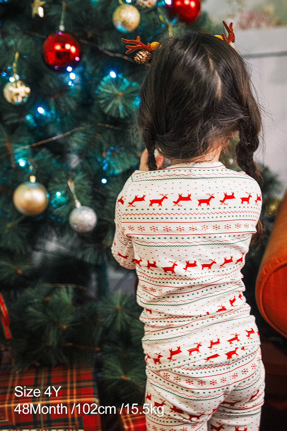 Back view of a child decorating Christmas tree, wearing AVAUMA Holiday Long Sleeve Pajama Set - Little Reindeer