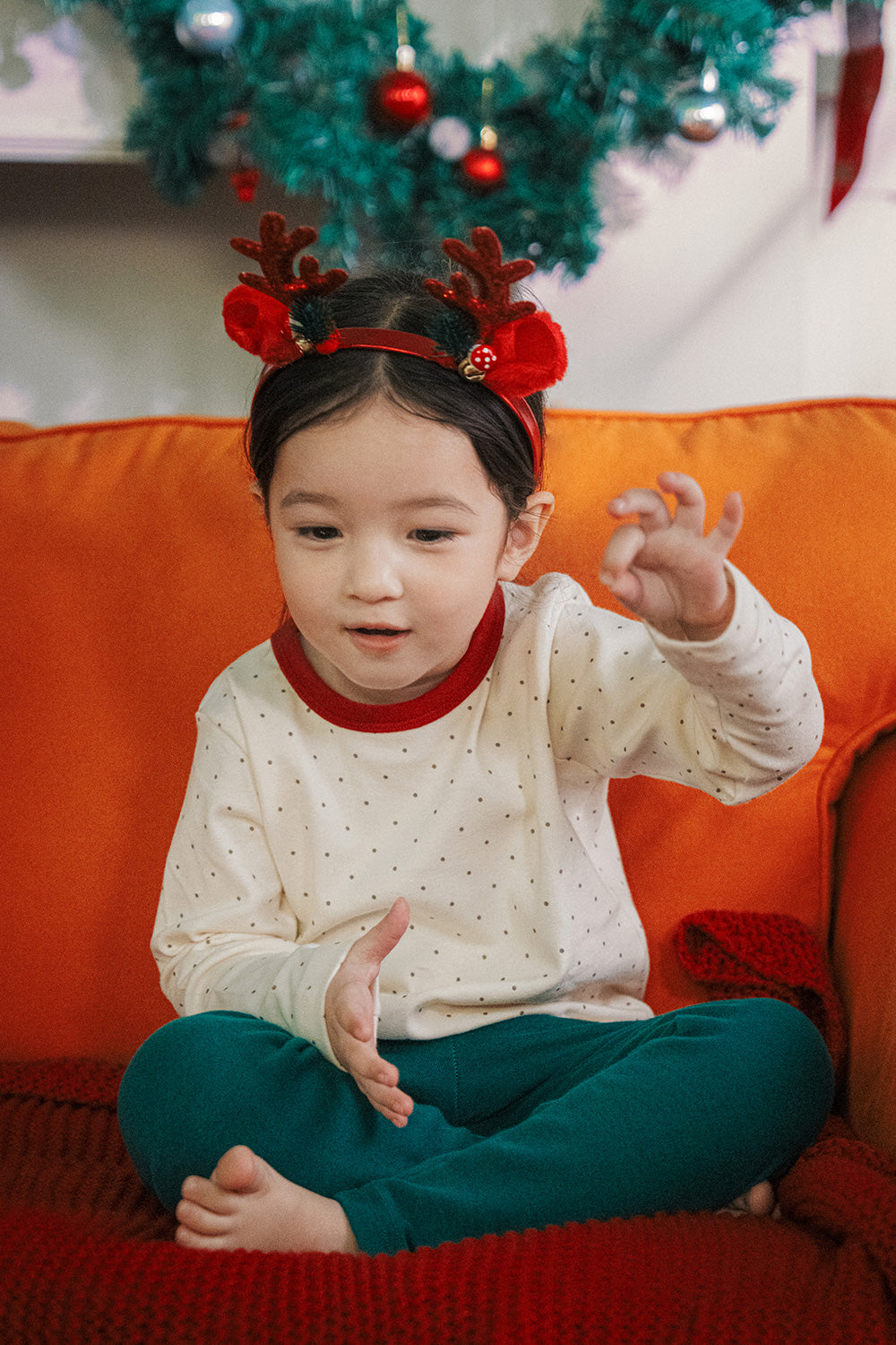 Toddler wearing Avauma holiday pajama set with red trim and polka dots, holding a red ornament. Ideal sleepwear for Christmas festivities.

