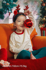 Toddler girl smiling and wearing Avauma holiday pajama set with reindeer antler headband, holding a red Christmas ornament. Festive sleepwear for holiday cheer.