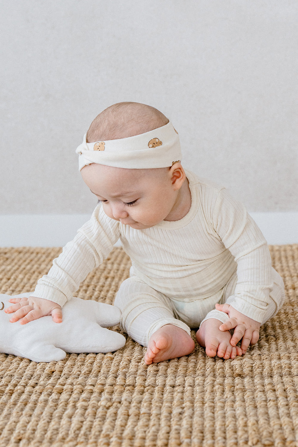 Infant sitting in Avauma Pogny Long Sleeve Set in Cheese Cake color, soft cotton sleepwear for baby's comfort, wearing a headband with bear pattern