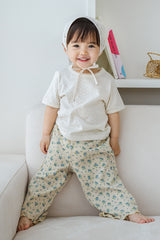 Smiling toddler in Avauma milk pearl lace short sleeve tee and flower print pants, standing on sofa

