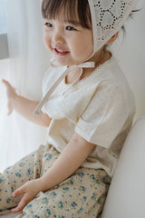 Happy toddler in Avauma milk pearl lace trim t-shirt and flower pants, sitting by window


