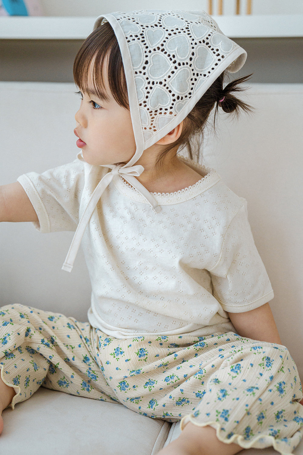 Side view of toddler girl in Avauma milk pearl lace short sleeve tee and heart lace bonnet

