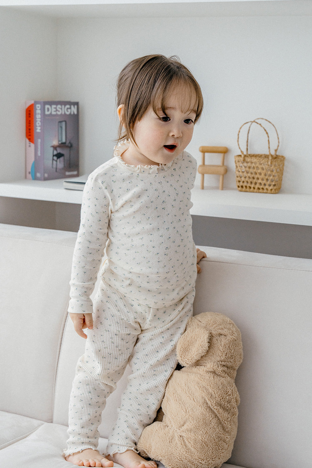 Baby standing in a crib wearing Avauma Eyelet Bloom Setup Pajamas - Creamy Flower, highlighting the ruffle neck details and the soft, floral design of the matching top and bottom.