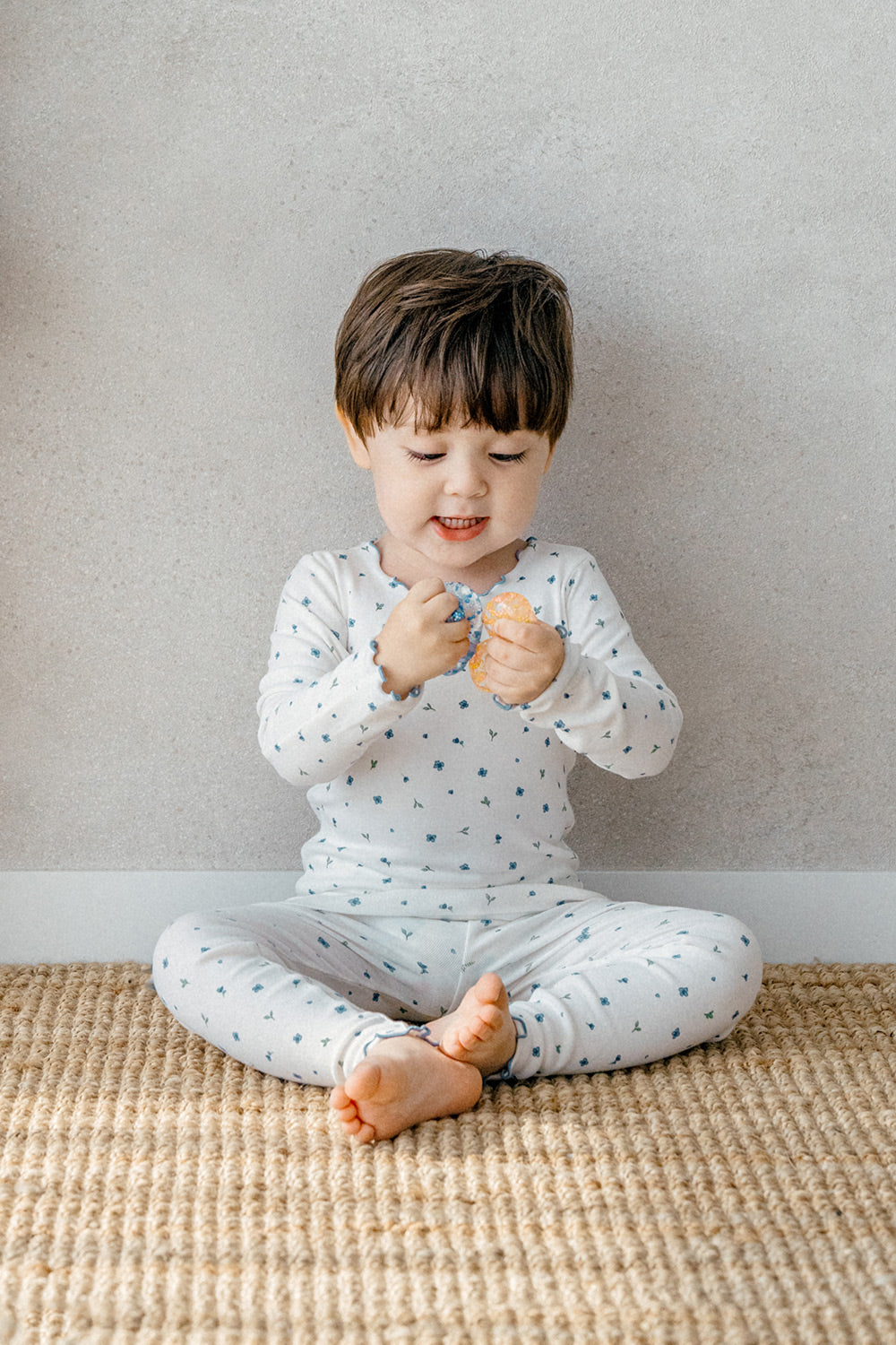 Toddler in Avauma Mini Fleur Long Sleeve Set - Frill Blooming, a cozy white pajama set adorned with blue flowers, designed for both comfort and style.