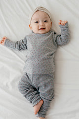 Smiling baby wearing Avauma Eyelet Bloom Setup - Gray Bloom, a soft gray pajama set with floral prints and ruffle accents, perfect for baby sleepwear.
