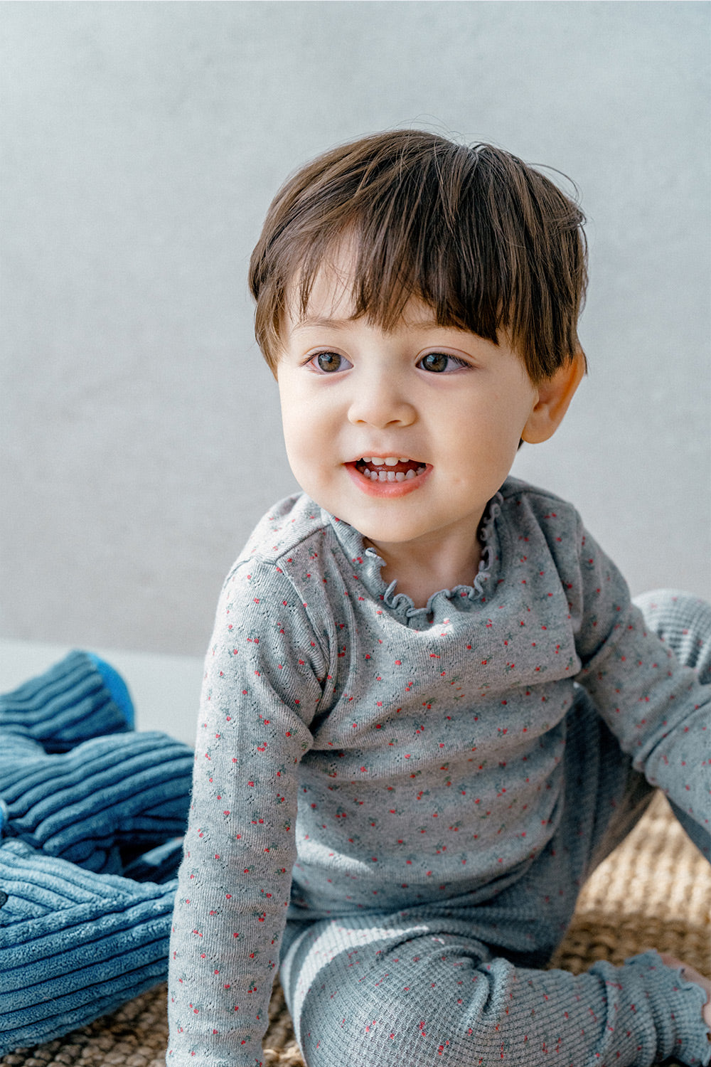 Toddler sitting while wearing Avauma Eyelet Bloom Setup - Gray Bloom, showing the playful floral print on the cozy pajama set.