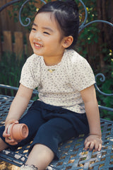 Little girl sitting on a bench in Avauma deep navy ruffle leggings and floral top, cozy 100% cotton outfit for toddlers.