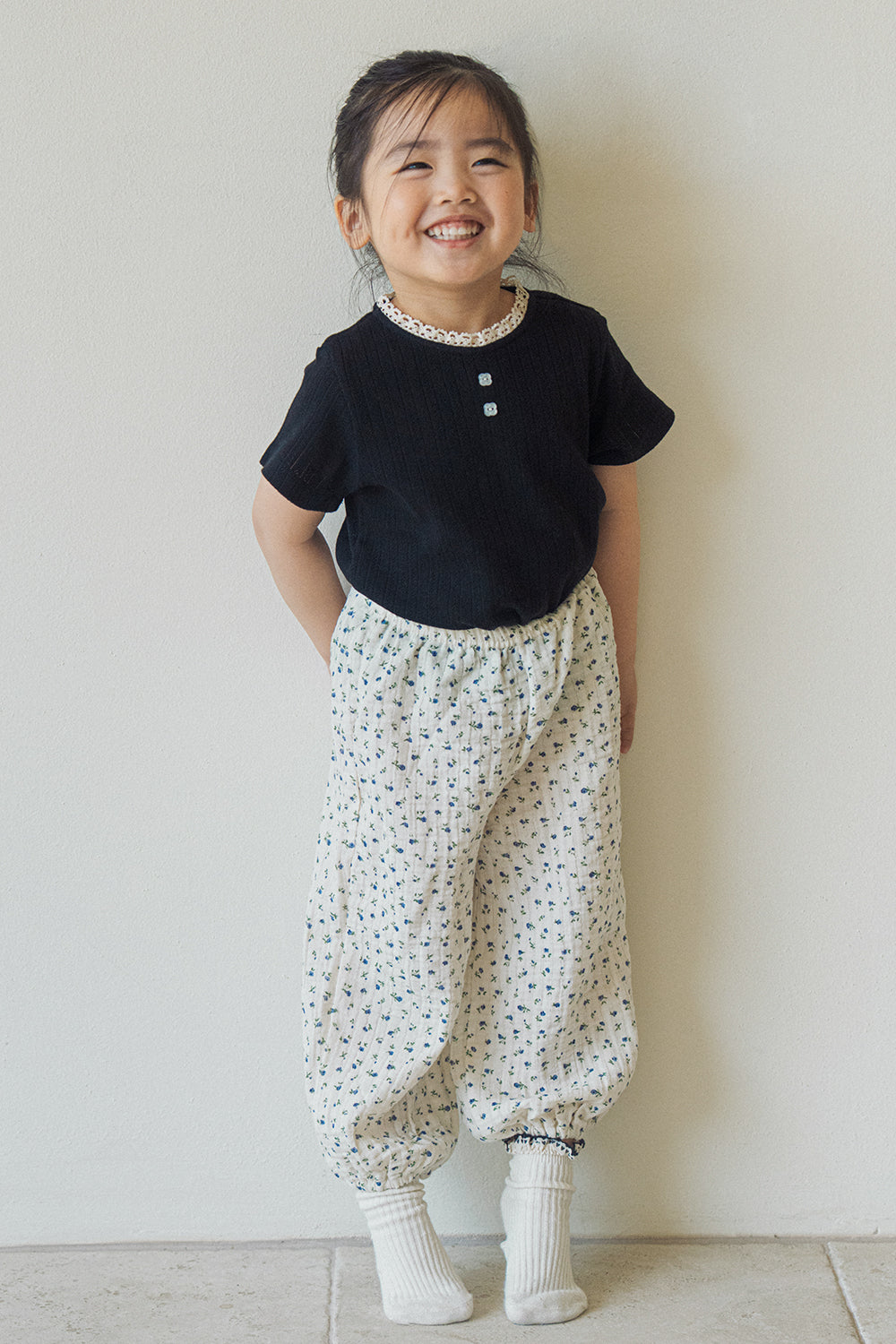 Full body shot of a smiling toddler modeling Avauma 100% cotton floral jogger pants and black tee, comfortable daily wear for ages 1-3.