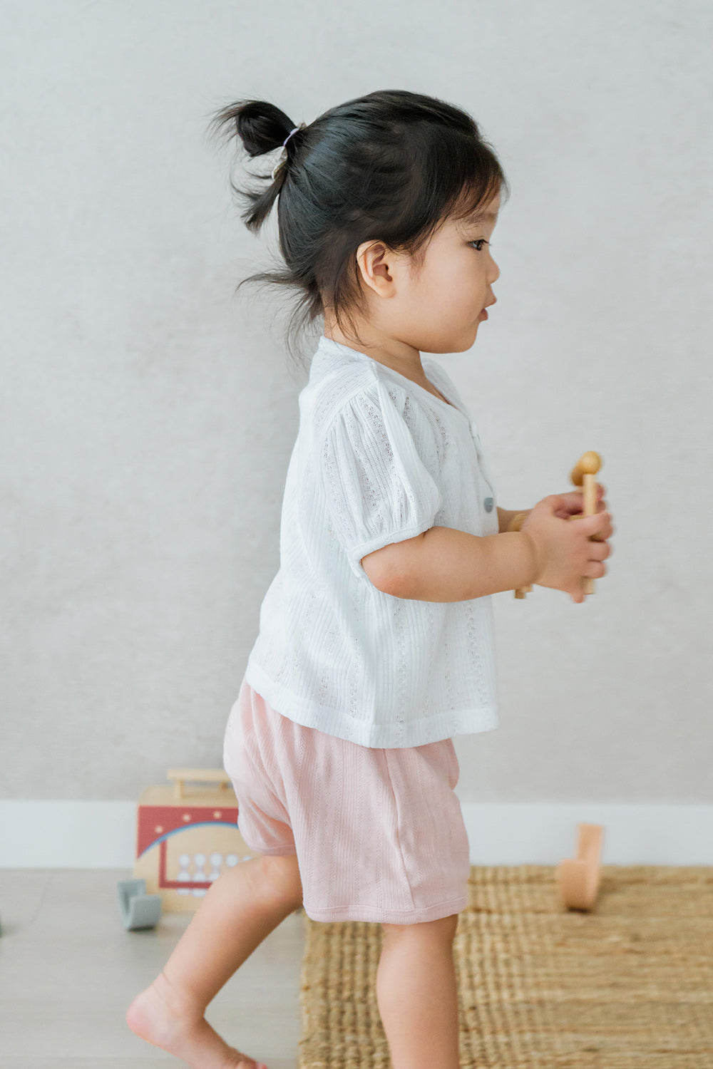 Baby walking indoors in Avauma Buttercumin cardigan in cotton ivory.

