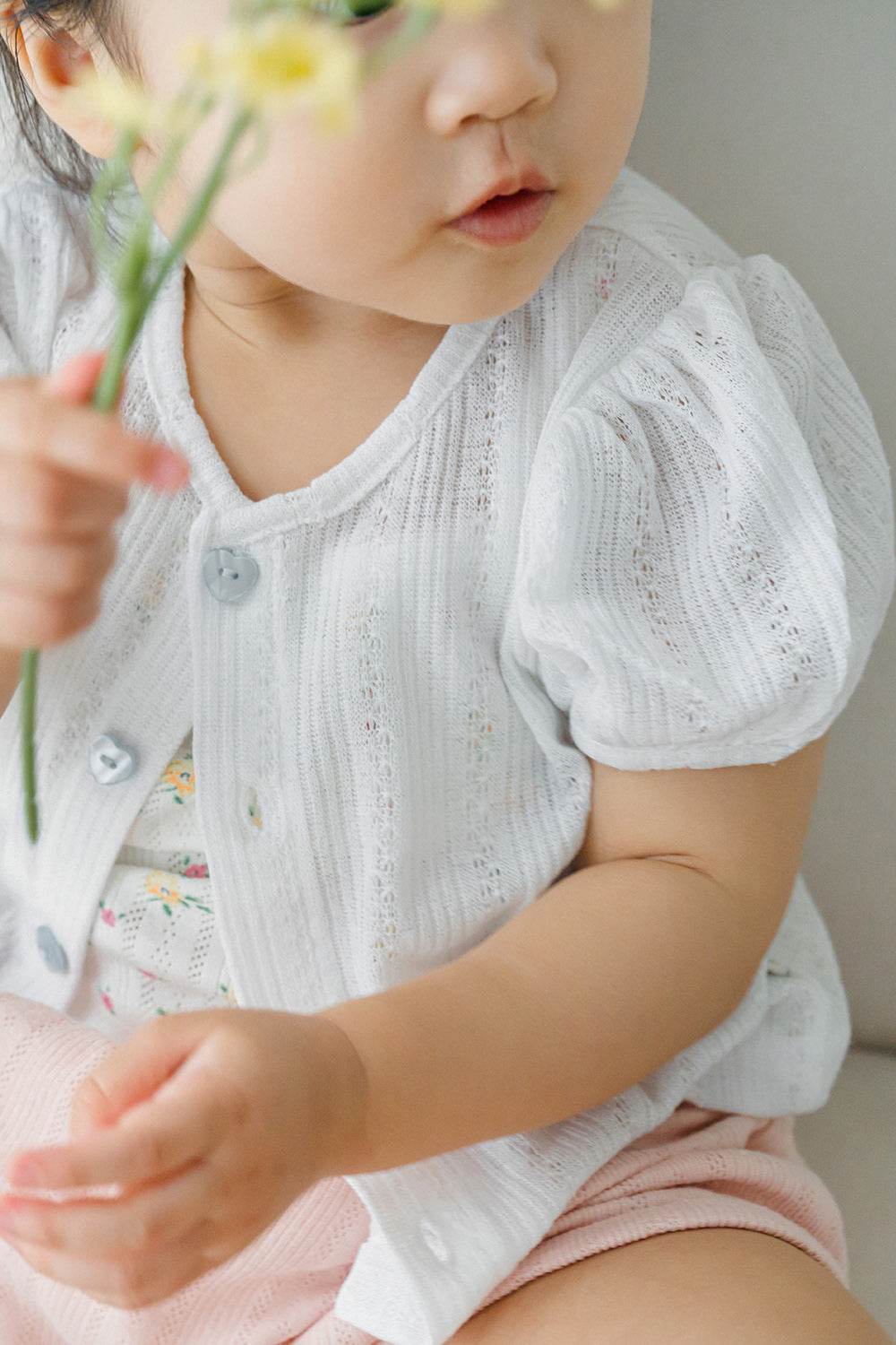 Close-up of baby wearing Avauma Buttercumin ivory cardigan and holding a flower.

