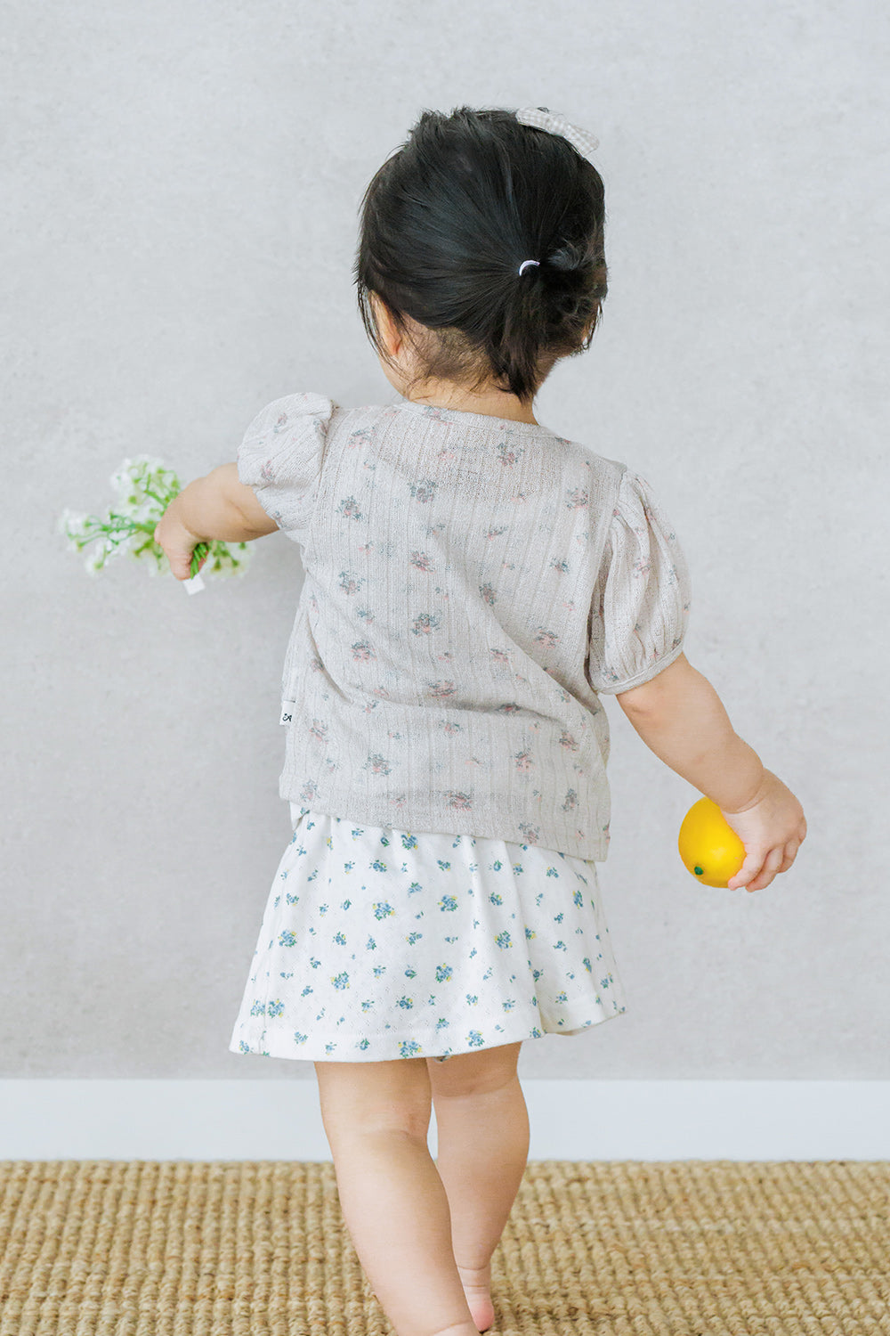 Toddler walking with flower and orange while wearing Avauma Buttercumin sand floral cardigan.

