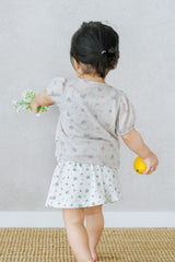 Toddler walking with flower and orange while wearing Avauma Buttercumin sand floral cardigan.


