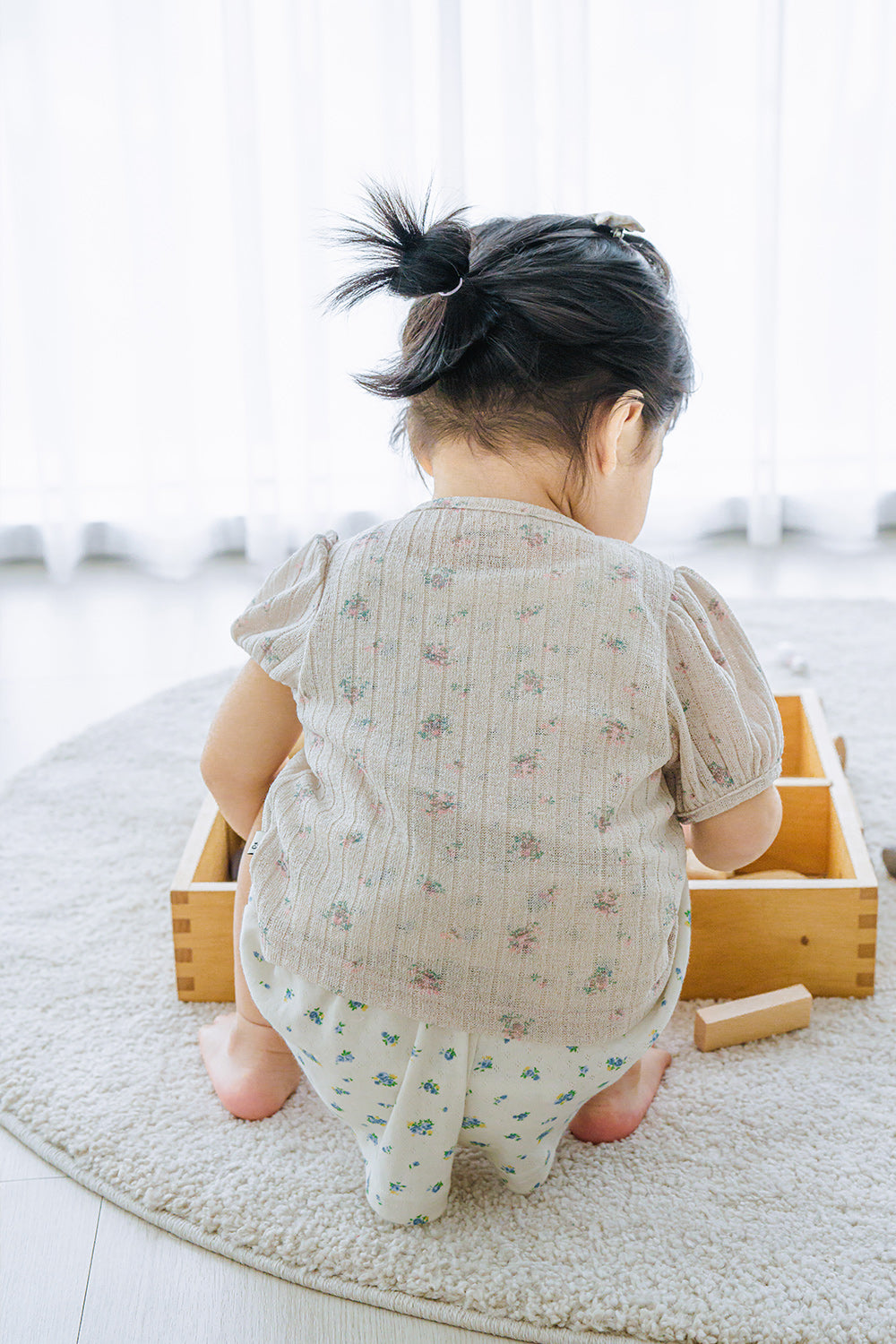 Baby playing with wooden blocks in Avauma Buttercumin cardigan, sand floral pattern.

