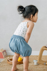 Toddler wearing Avauma Linen Bloomer Sky. Child in a floral tank top and light blue linen bloomers, standing barefoot.