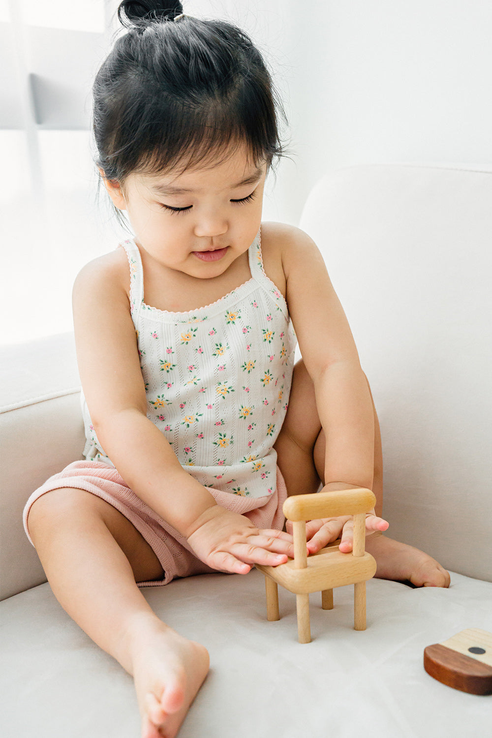 Toddler sitting and playing in Avauma apricot daisy tank top and pink shorts
