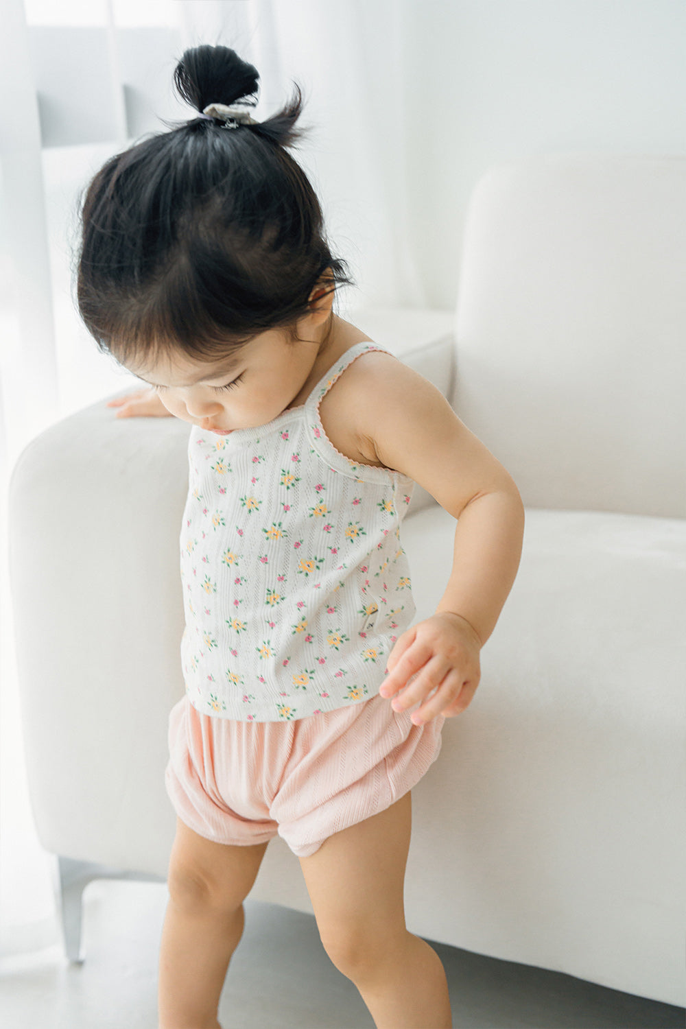 Child standing in Avauma apricot daisy tank top and pink shorts, looking down