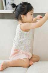 Side view of child sitting on sofa in Avauma apricot daisy tank top and pink shorts