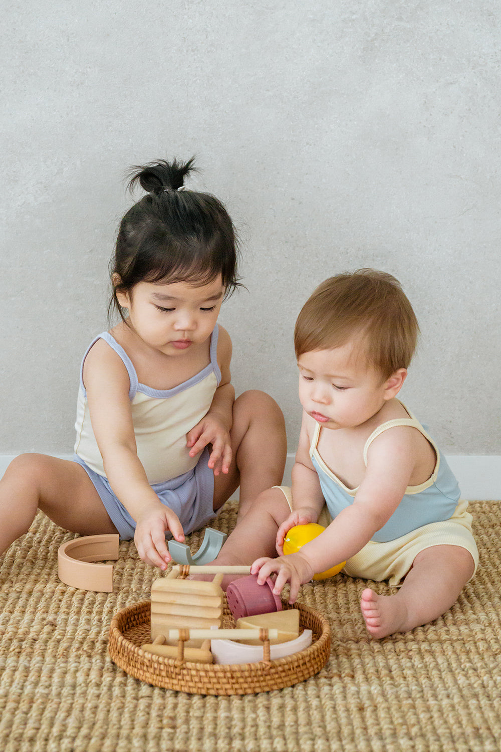 Two babies wearing AVAUMA Laila Day sleeveless sets, sitting on floor and playing with toys