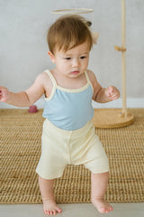 Baby wearing Avauma pale lime sleeveless set, standing on woven mat
