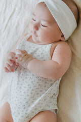 Sweet baby in Avauma Lily Sleeveless Bodysuit Cream Blue. Newborn lying down with closed eyes, wearing a cream and blue floral print romper and white headband.

