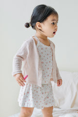 Toddler girl wearing avauma Little Shell Cardigan – Almond Cream over a floral dress, standing indoors.