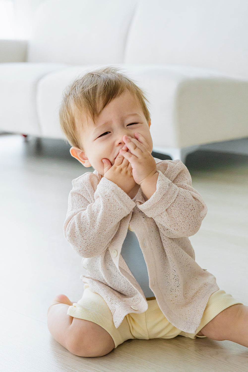 Baby sitting and smiling while wearing Avauma Littleshell cardigan in almond cream over a beige romper.

