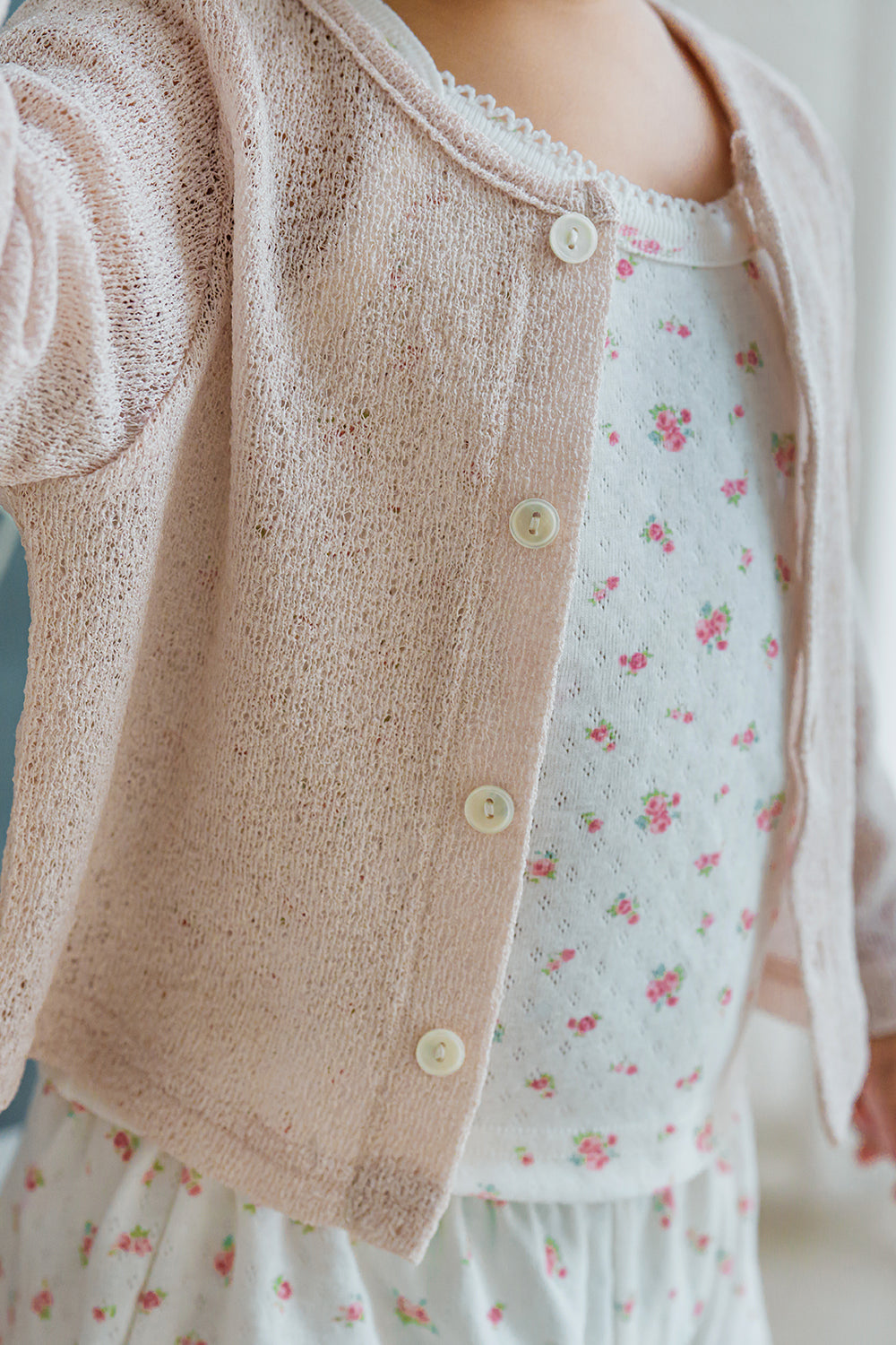 Close-up of Avauma Littleshell almond cream cardigan layered over floral dress.

