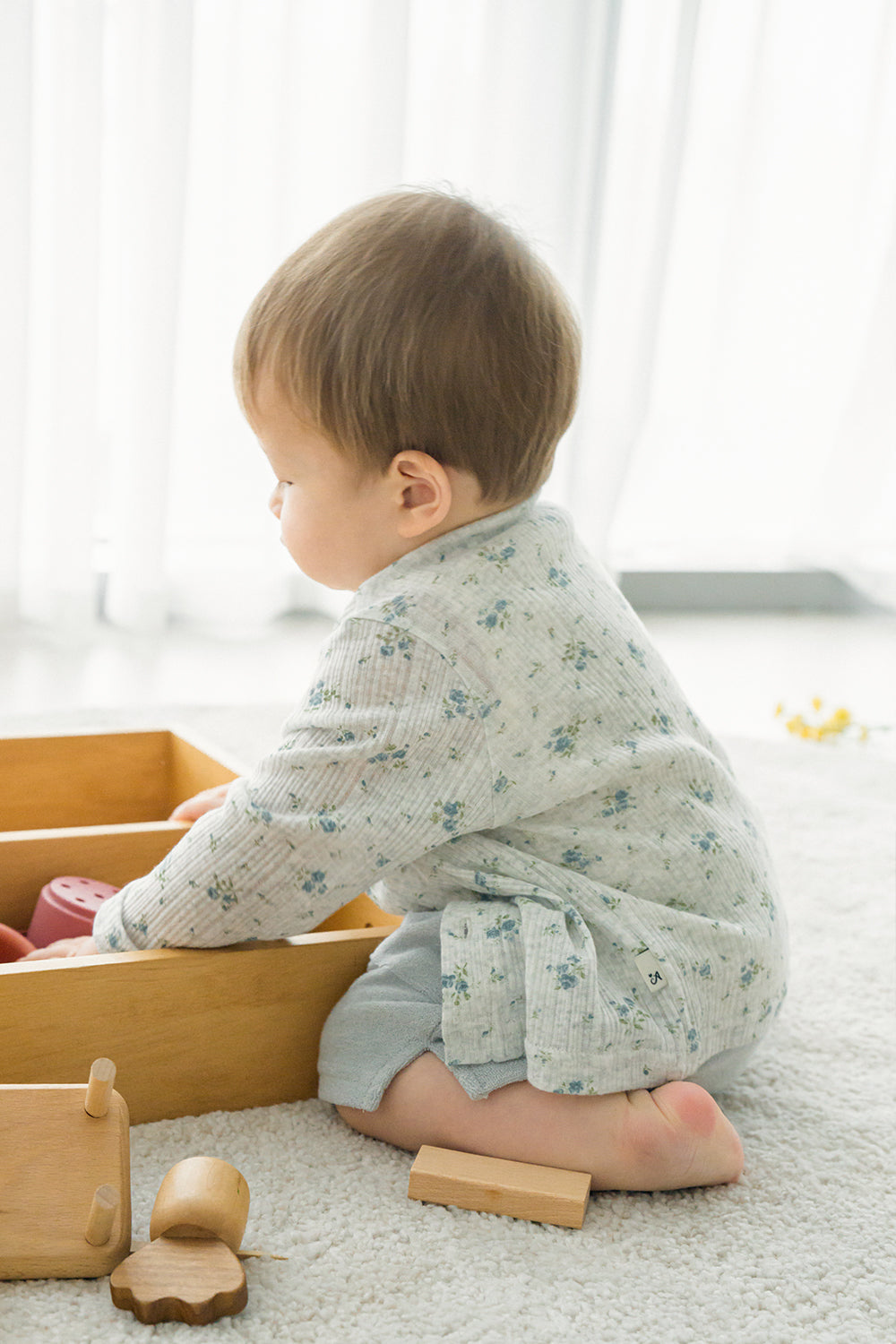 Baby playing with wooden toys while wearing Avauma Littleshell cardigan in forest mint.

