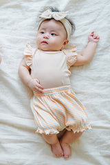  Adorable baby wearing Avauma Mellow Stripe Set Peach Macaron. Infant lying down in a soft peach bodysuit and striped bloomers with a matching headband.