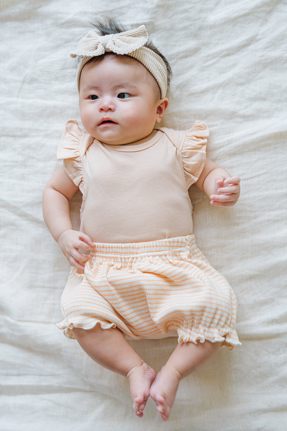 Cute newborn in Avauma Mellow Stripe Set Peach Macaron. Baby lying flat, showcasing the gentle peach bodysuit and striped bloomers.