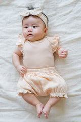 Cute newborn in Avauma Mellow Stripe Set Peach Macaron. Baby lying flat, showcasing the gentle peach bodysuit and striped bloomers.