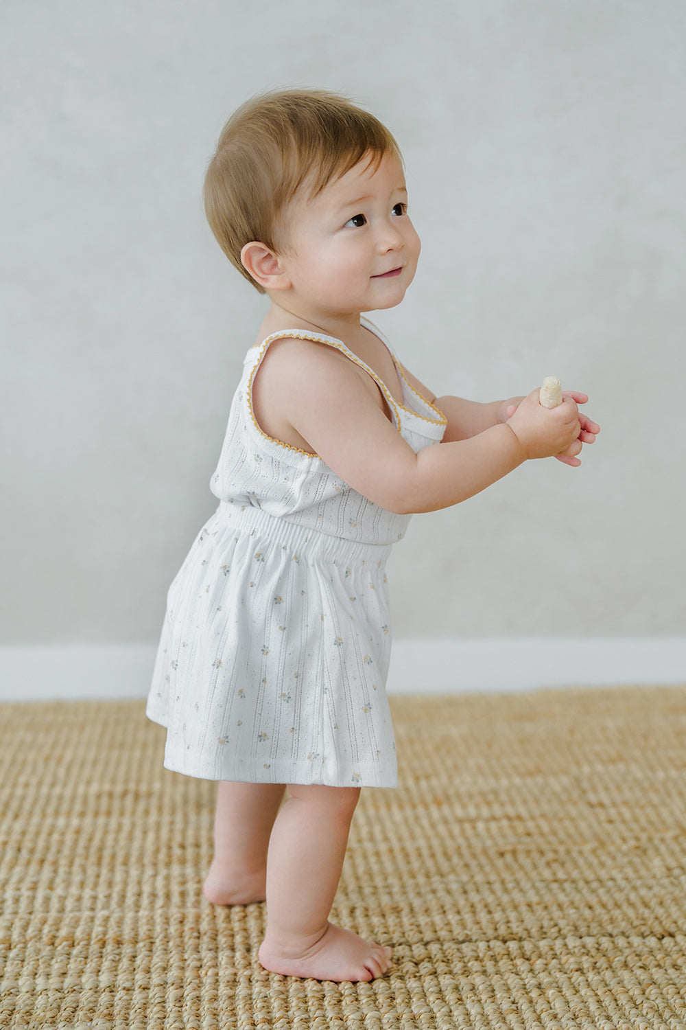 Baby in Avauma Butter Daisy tank top set, standing on a woven mat
