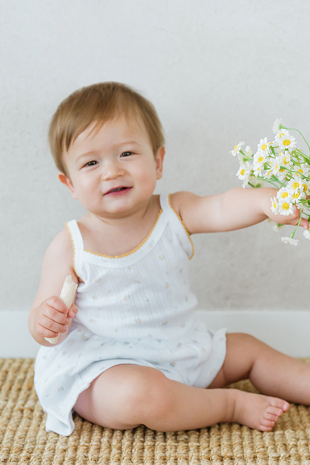 Smiling baby holding a flower in Avauma Butter Daisy tank top set

