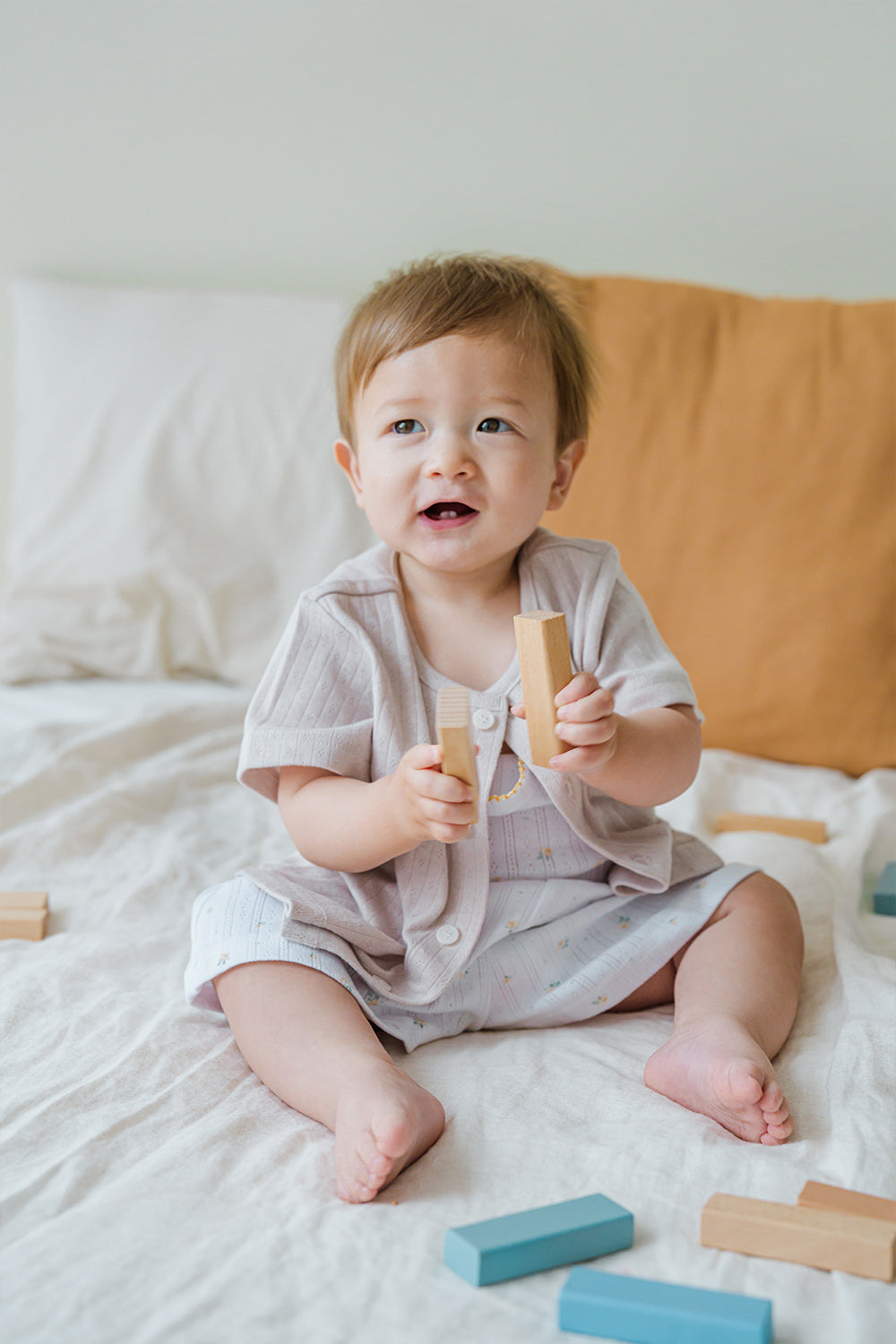 Toddler wearing Avauma picnic tank top set in Blue Herb pattern, holding a toy on a bed

