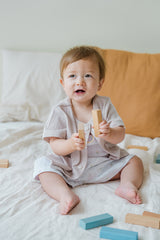 Toddler wearing Avauma picnic tank top set in Blue Herb pattern, holding a toy on a bed
