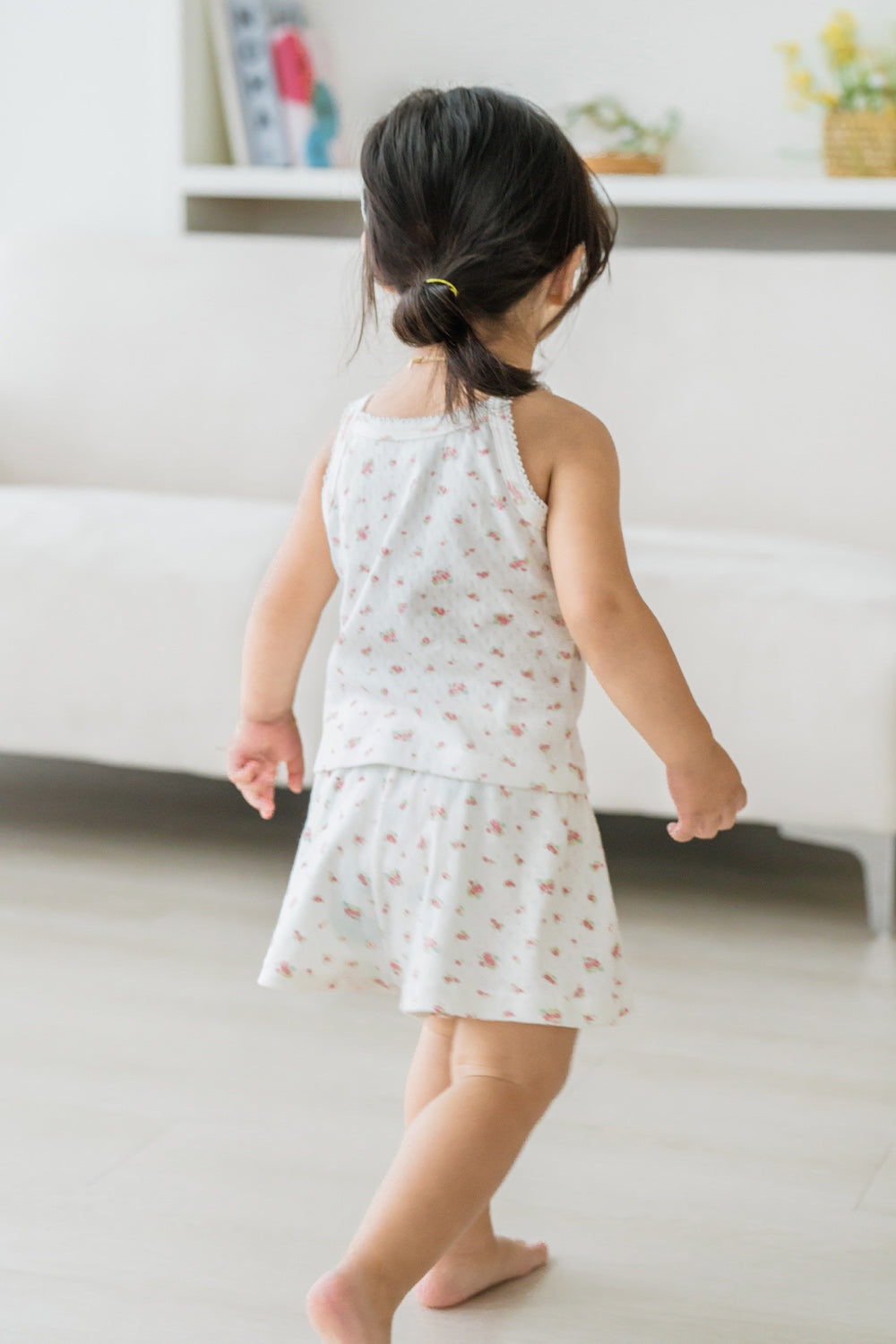 Back view of toddler wearing Avauma rose belle sleeveless picnic set, walking on white rug